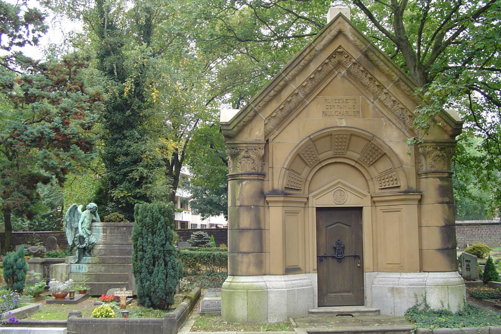 Blick auf eine Grabstätte auf dem Friedhof Mühlheim, daneben grüne Bäume und eine Engelsstatur.