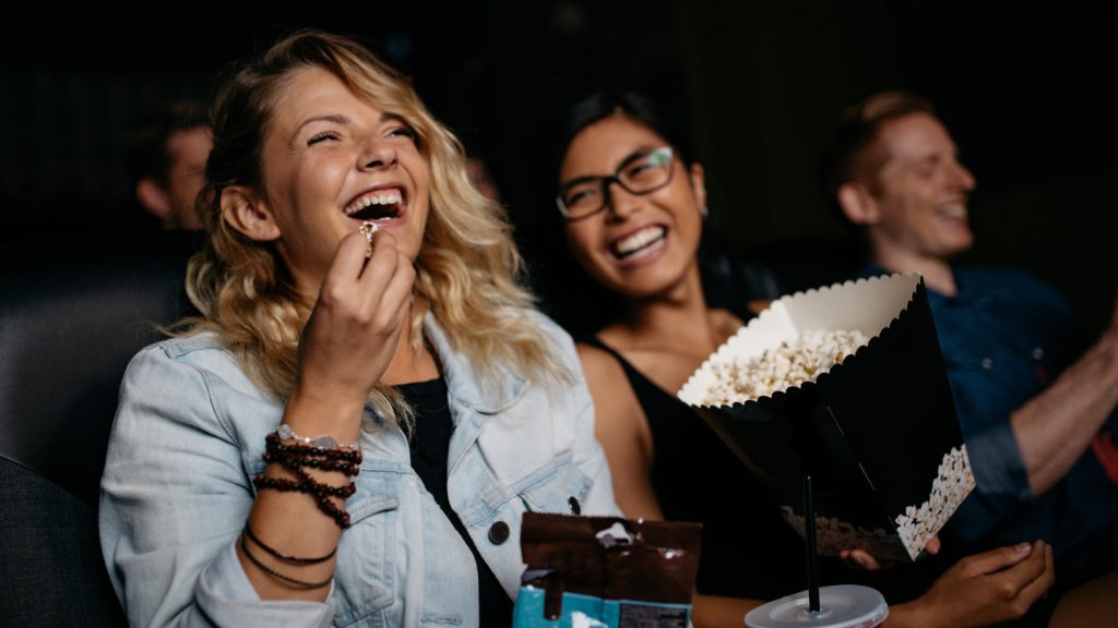 Junge Frau mit Freunden beobachten Film im Kino und lachen. Gruppe von Menschen im Theater mit Popcorns und Getränke.