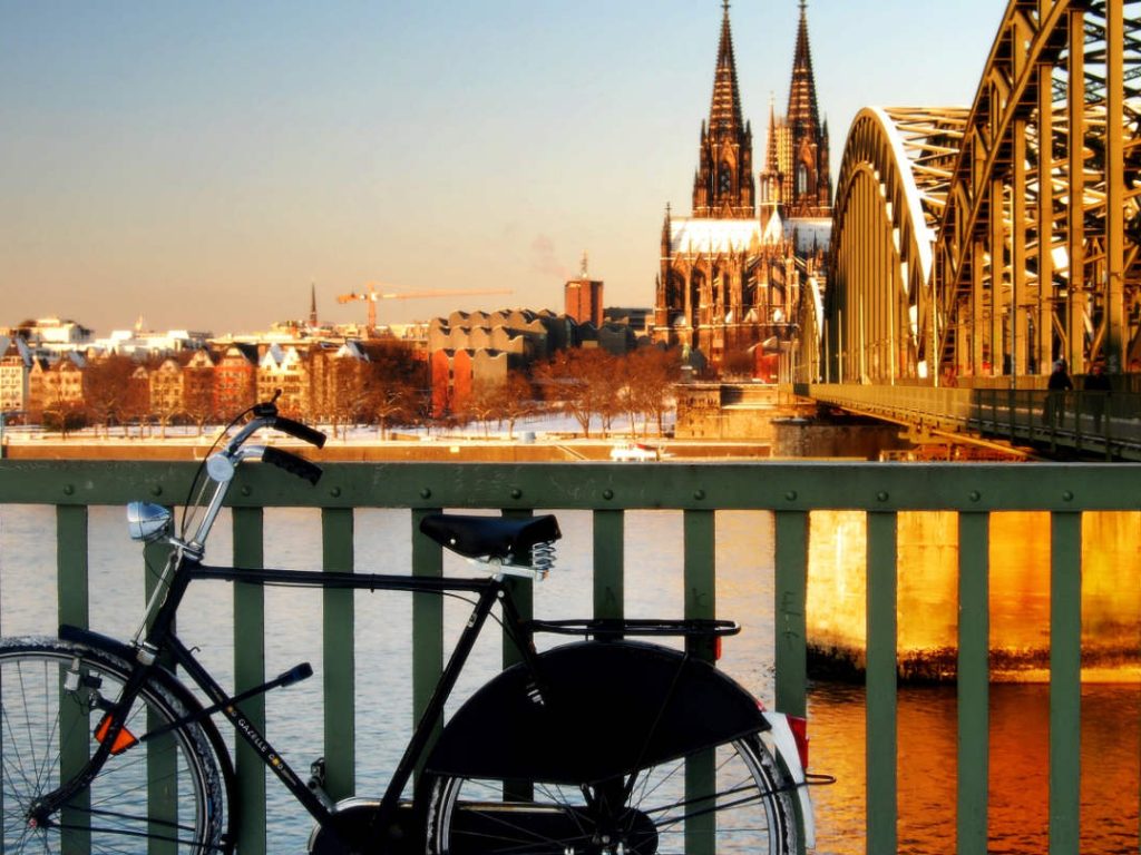 Fahrrad am Zaun in der Nähe der Eisenbahnbrücke in Köln mit dem Dom im Hintergrund.