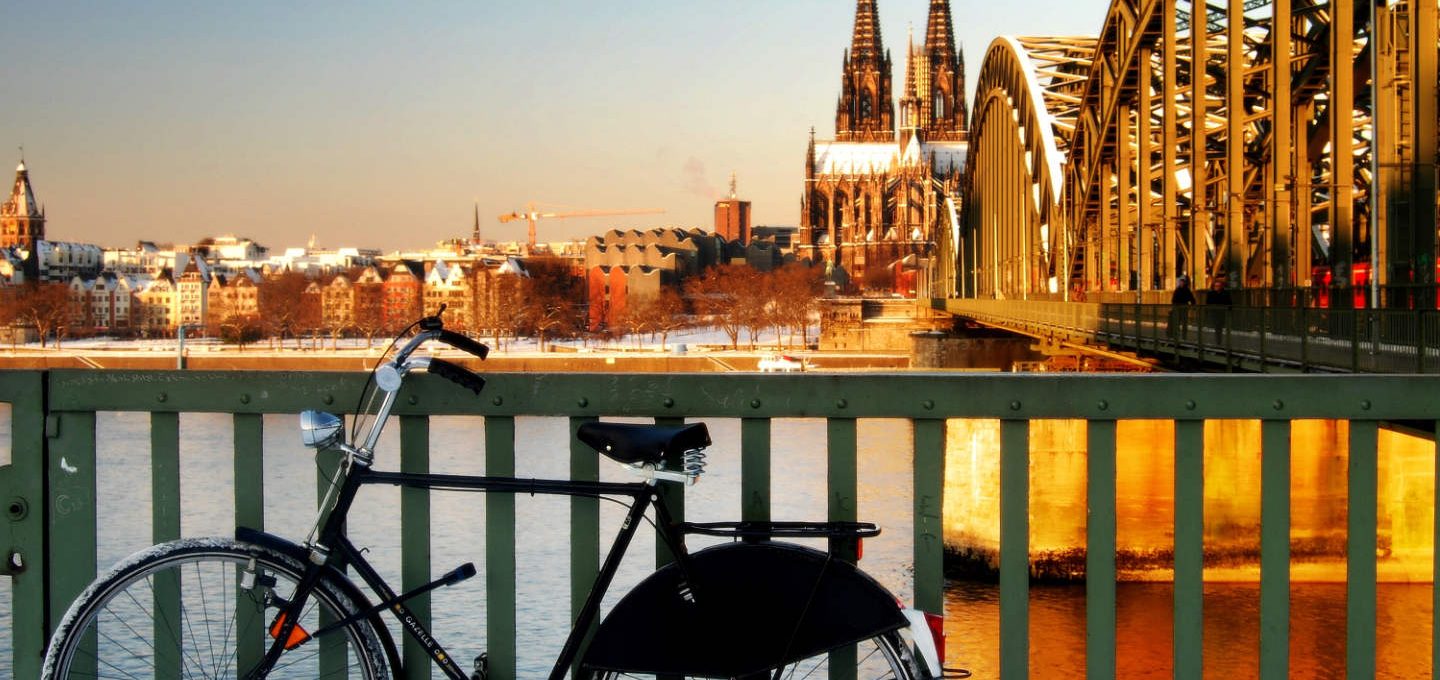 Fahrrad am Zaun in der Nähe der Eisenbahnbrücke in Köln mit dem Dom im Hintergrund.