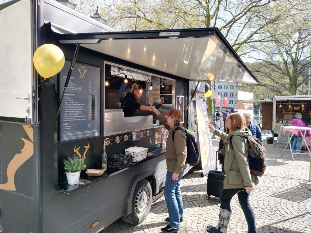 Streetfood in Köln: Ein Burger-Truck auf einem Marktplatz, an dem Menschen sich Burger bestellen.
