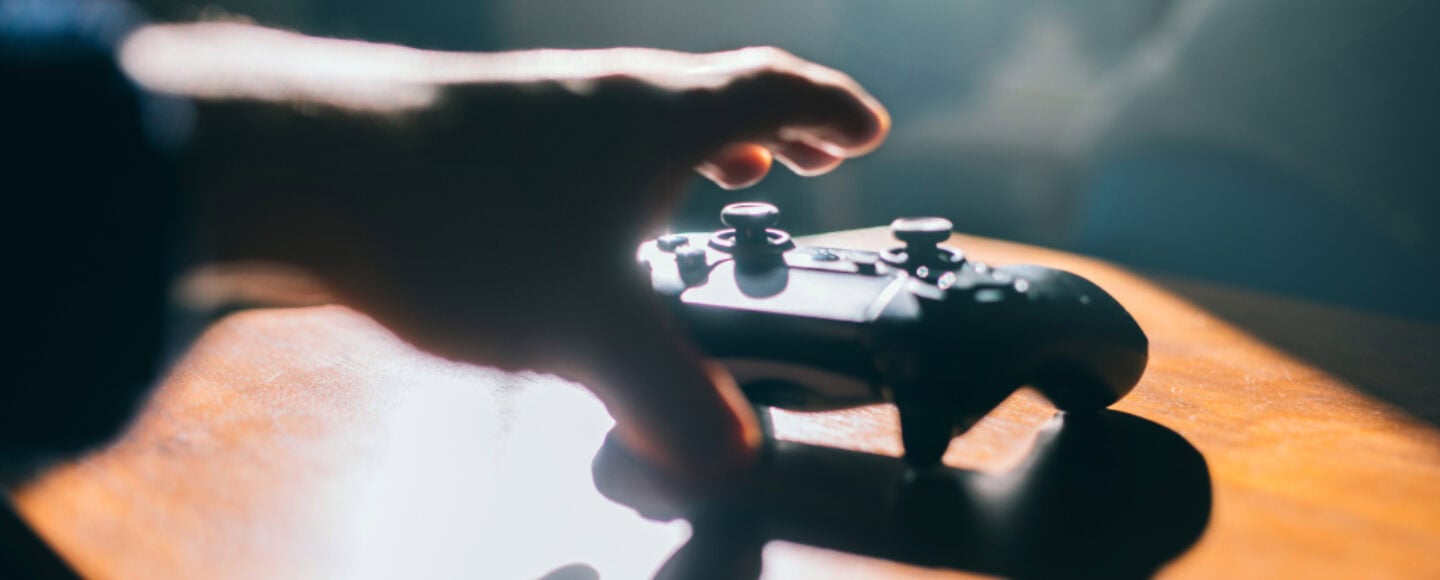 Hand greift nach schwarzem Gaming-Controller auf Holztisch im Sonnenlicht.